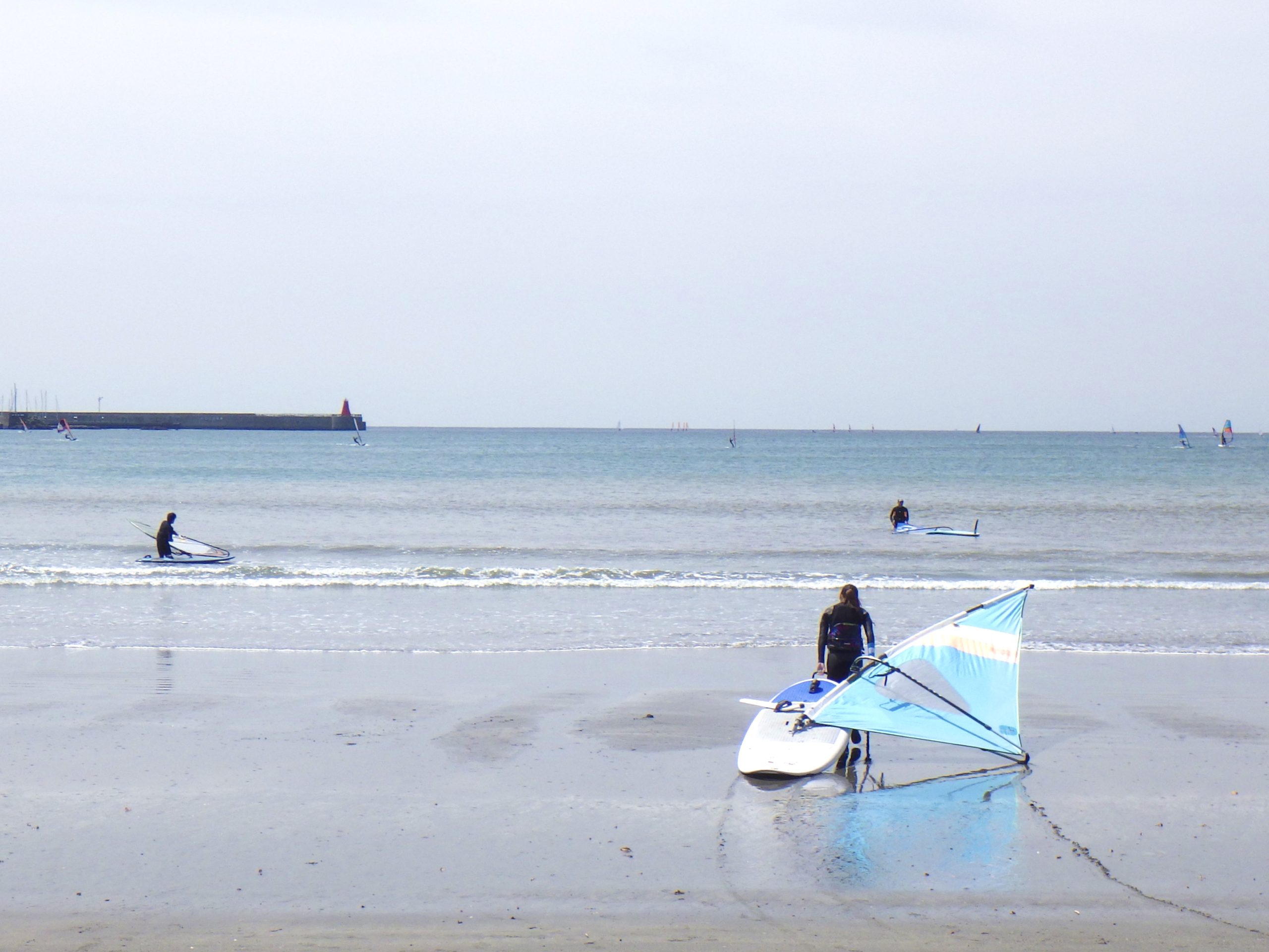 逗子海岸の波が少し入った風景。フェザーファクトリーのスクール道具を運んで海に向かって行きます。